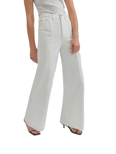 Studio photograph of a model wearing high-waisted white wide-leg jeans featuring front vertical seams and brown strappy heels against a minimalist white background