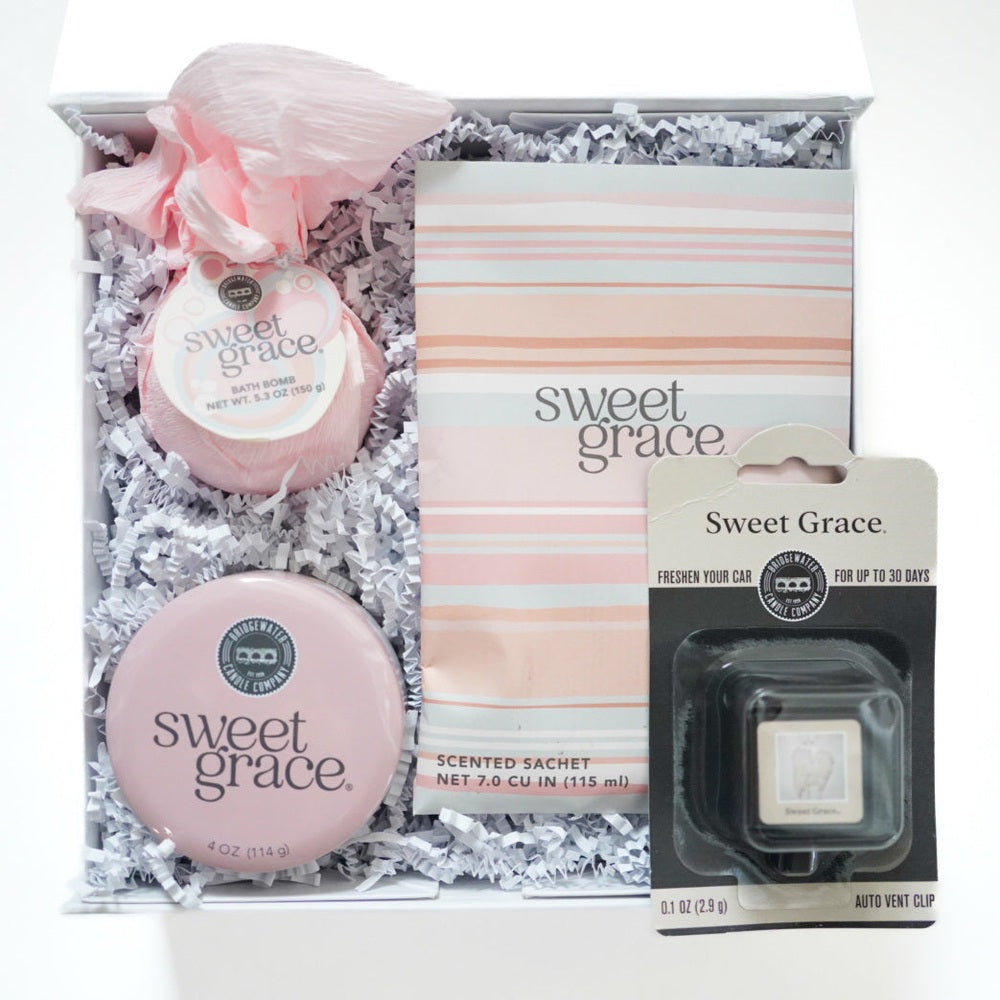 Photograph of Bridgewater Candle Company’s Sweet Grace gift set featuring a pink tissue-wrapped bath bomb, a striped scented sachet, and a round pink tin nestled in white crinkle paper