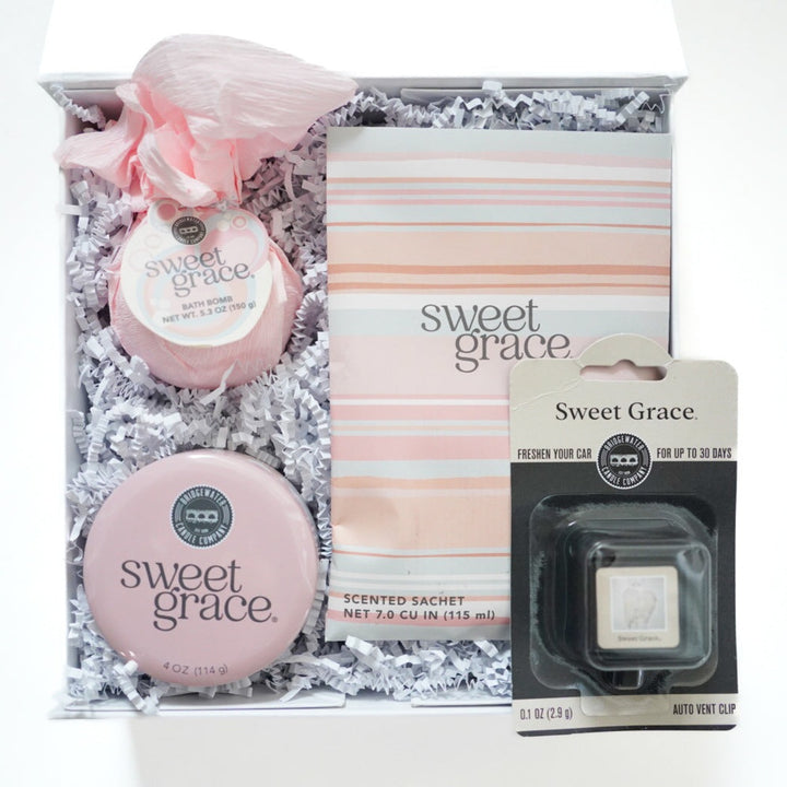 Photograph of Bridgewater Candle Company’s Sweet Grace gift set featuring a pink tissue-wrapped bath bomb, a striped scented sachet, and a round pink tin nestled in white crinkle paper