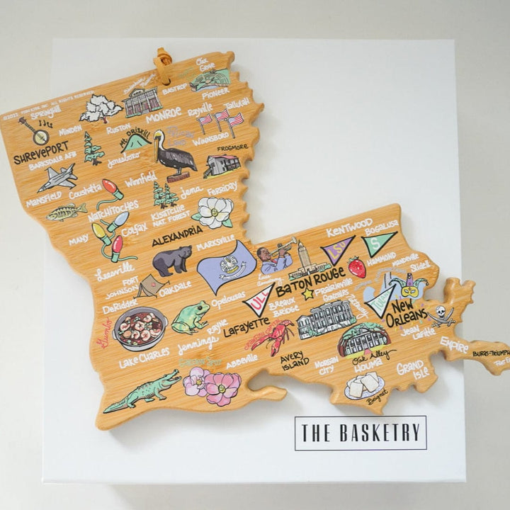 Illustrated bamboo cutting board by Fish Kiss depicting a colorful map of Louisiana featuring landmarks like the State Capitol in Baton Rouge and New Orleans alongside vibrant illustrations of a red crawfish, a green alligator, and a steaming bowl of gumbo