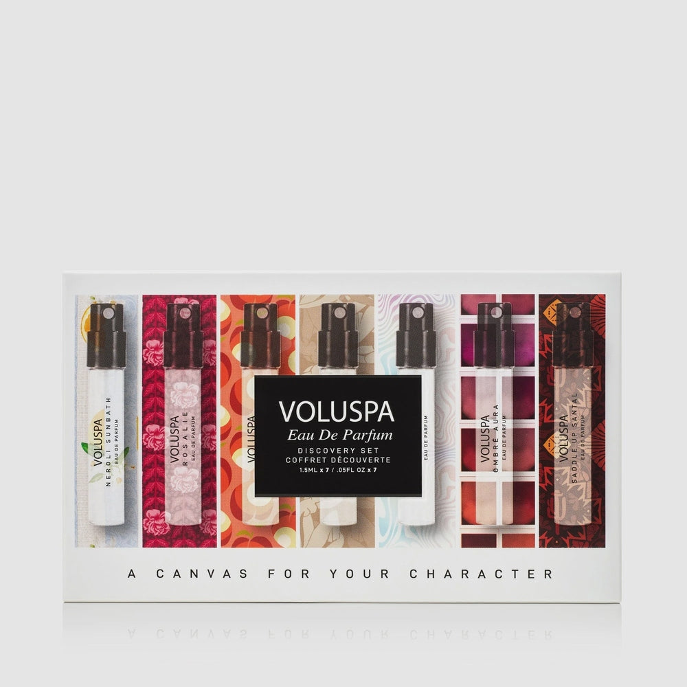 Studio product photograph of the Voluspa Eau De Parfum Discovery Set displaying seven glass vials against vibrant floral and geometric patterned backgrounds with a central black label and the tagline A CANVAS FOR YOUR CHARACTER