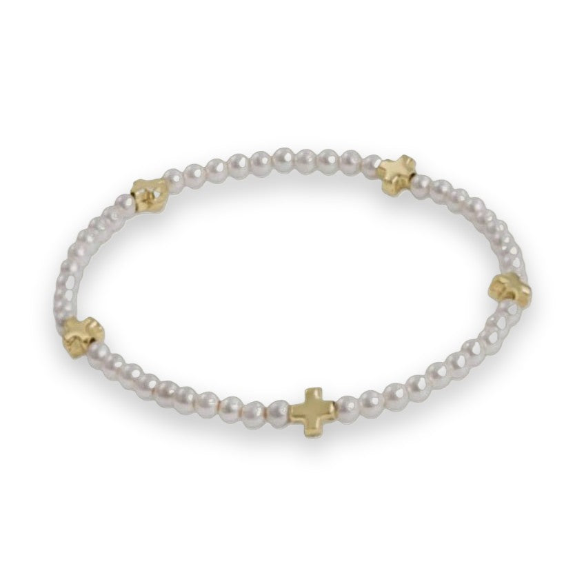 Beaded jewelry featuring a dainty bracelet of small lustrous white pearls interspersed with five polished gold-tone cross charms on a neutral gray background