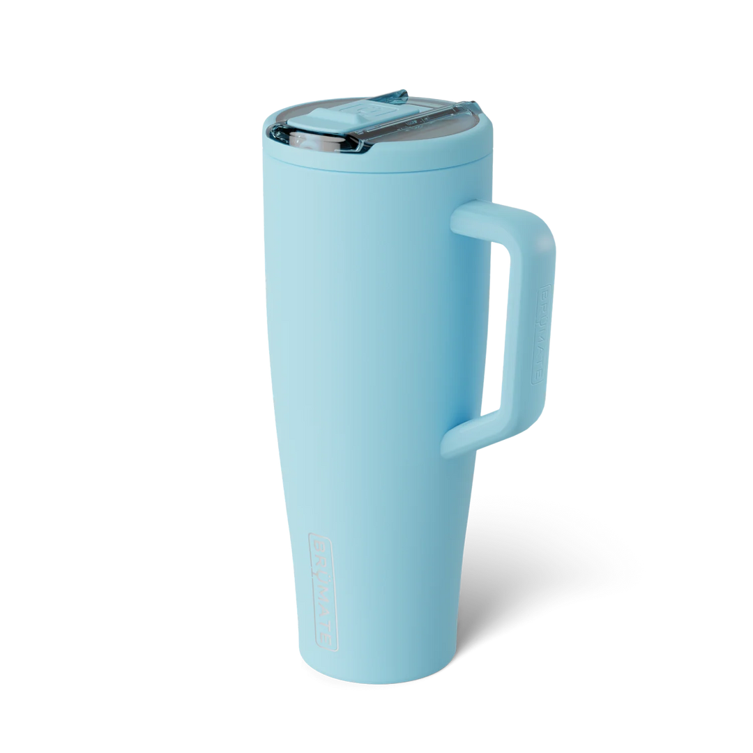 Product photography by BrüMate of an Era tumbler featuring a matte sky blue finish, an integrated side handle with embossed branding, and a transparent flip-top lid set against a white background