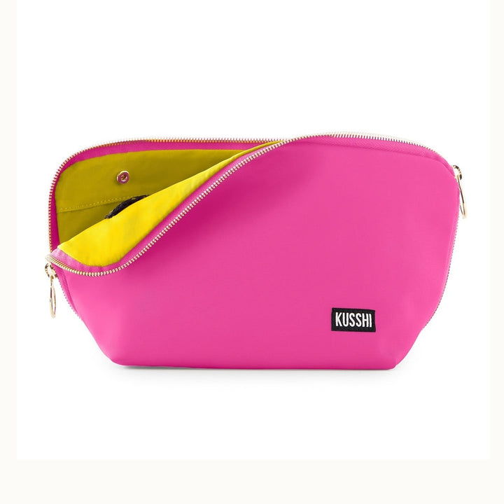 Product photograph by Kusshi of a hot pink makeup bag in a studio setting featuring a contrasting lime green lining, gold-toned zipper pulls, and a black brand label