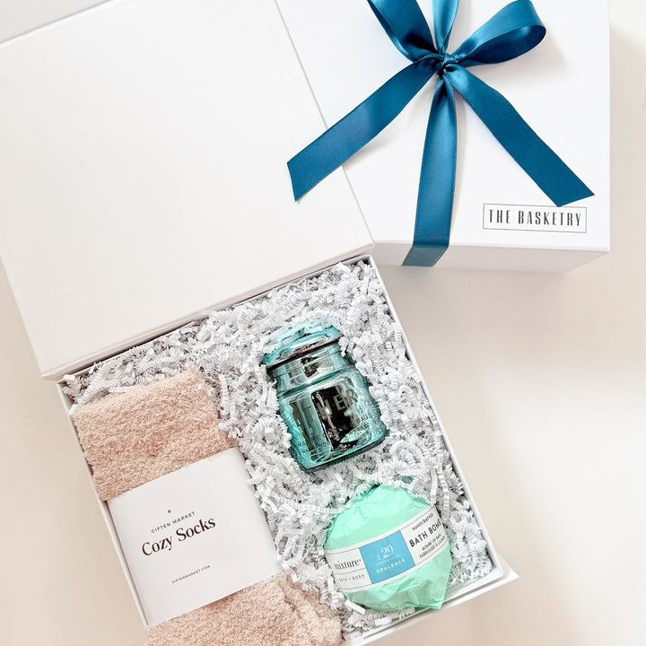 Gift set with bath items including a jar, ball, and socks in a box with a blue ribbon.