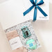 Gift set with bath items including a jar, ball, and socks in a box with a blue ribbon.