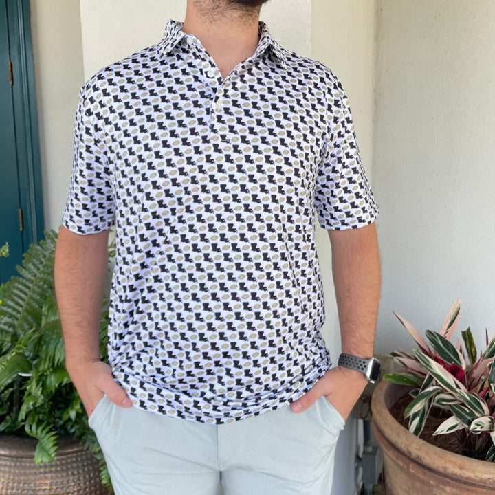 Man wearing a white polo printed with black Louisiana shapes and gold footballs, hands in pockets