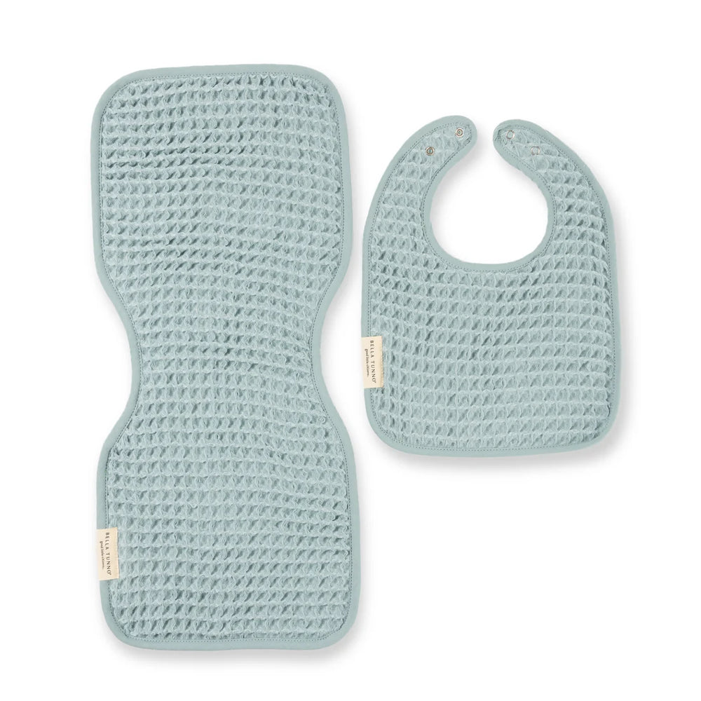Waffle knit fabric by Bella Tunno featuring a pale eucalyptus blue baby bib and matching contoured burp cloth set on a white background with prominent brand tags and a textured honeycomb weave