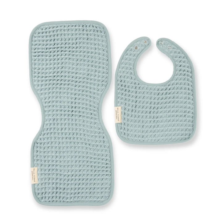Waffle knit fabric by Bella Tunno featuring a pale eucalyptus blue baby bib and matching contoured burp cloth set on a white background with prominent brand tags and a textured honeycomb weave