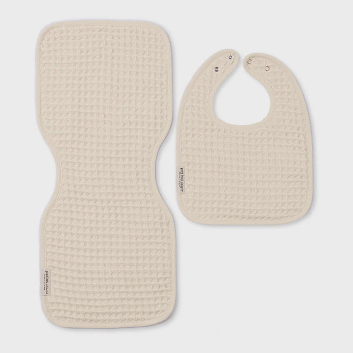 Waffle-knit cotton baby bib and burp cloth set by Bella Tunno displayed on a neutral studio background featuring Good Little Citizens brand labels, cream-colored textured weave, and silver snap closures
