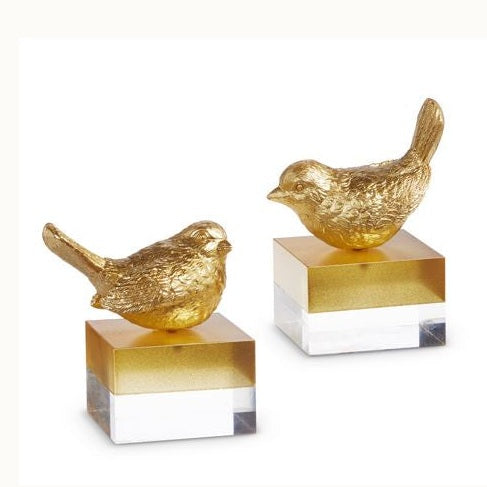 Gold-finished bird sculptures with textured metallic feathers and rounded bodies are mounted on square two-toned pedestals featuring clear acrylic bases against a white studio background