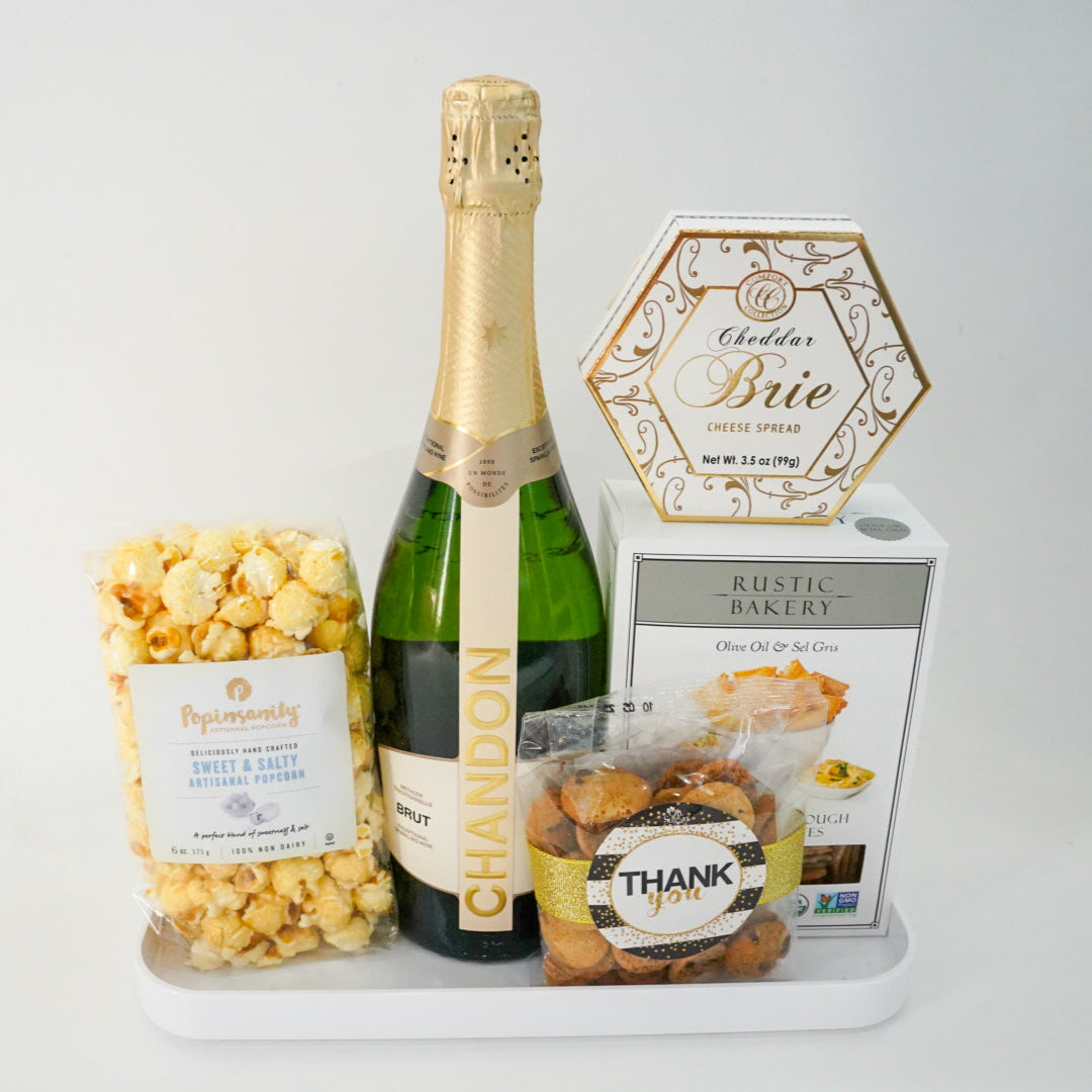 Bottle of champagne, popcorn, and a box of cookies on a white surface with a gray background