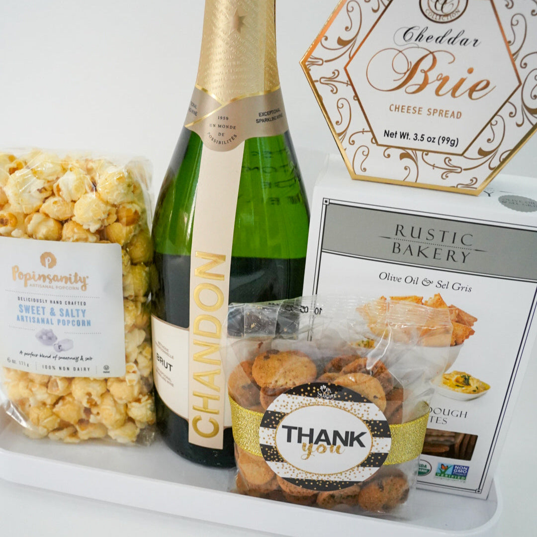 Bottle of champagne with popcorn, cheese, and crackers on a white surface