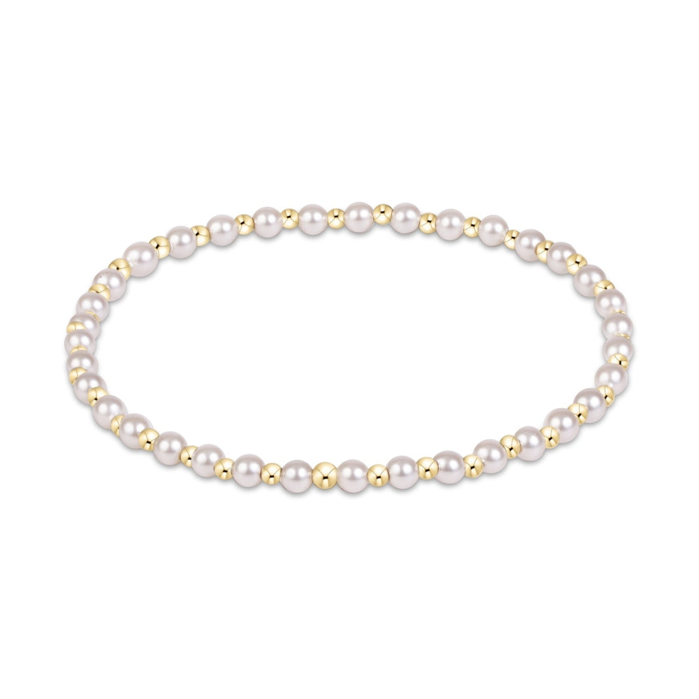 Jewelry photograph of a circular beaded bracelet on a white background featuring lustrous white pearls and small polished gold spheres in a repeating rhythmic pattern