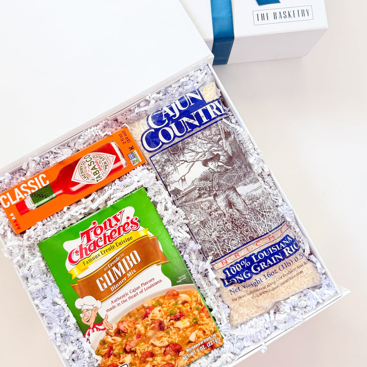 Digital photograph by The Basketry of a Louisiana-themed gift box featuring iconic red Tabasco sauce, bright green Tony Chachere’s Gumbo mix, and Cajun Country rice nestled in white crinkle paper