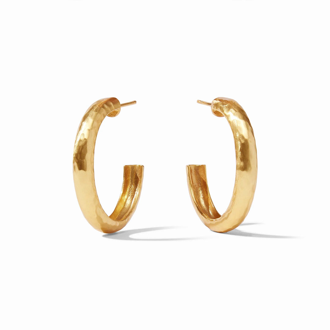 Gold-plated brass earrings featuring a pair of thick C-shaped hoops on a minimalist white background with a distinctive hammered surface and a high-shine golden luster