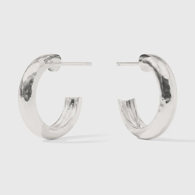 Handcrafted sterling silver jewelry featuring a pair of hammered hoop earrings on a minimalist studio background, highlighting a dimpled organic texture and polished metallic highlights with visible post-back pins