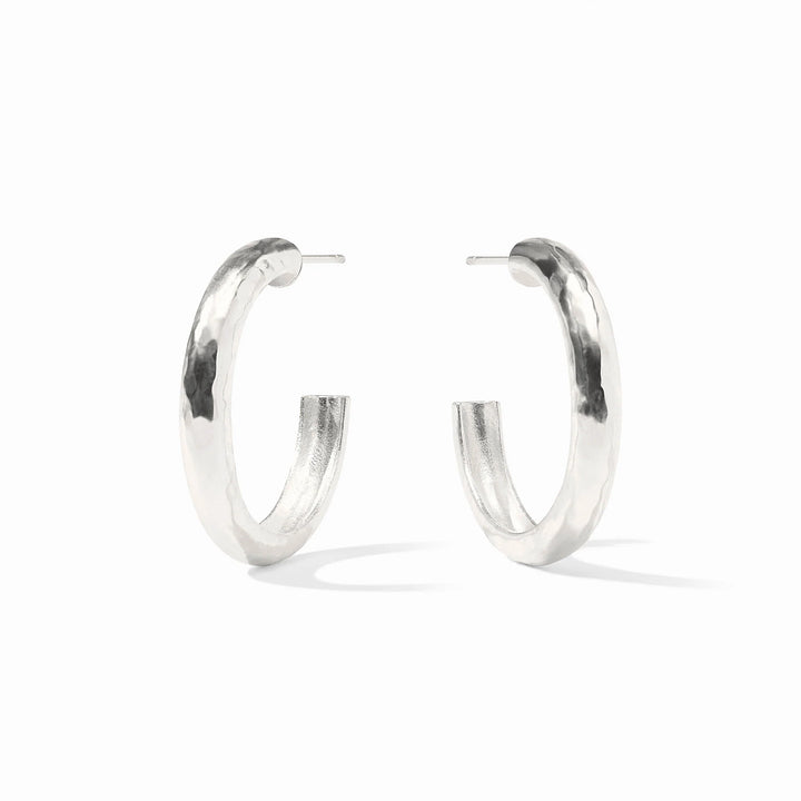 Sterling silver pair of thick hoop earrings on a white background featuring a unique hammered texture and a polished reflective finish