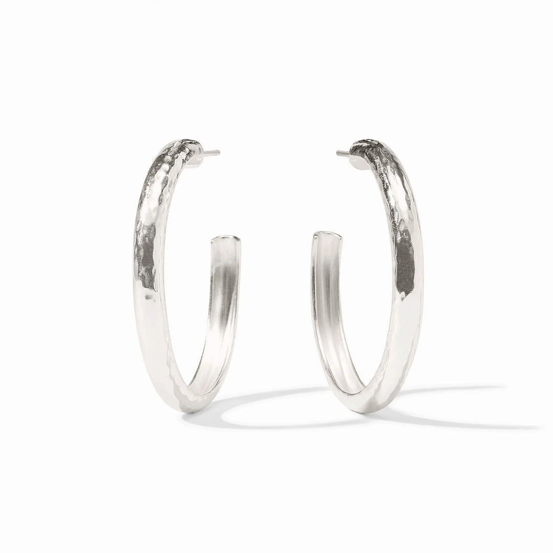 Sterling silver jewelry featuring a pair of large hoop earrings on a white studio backdrop showcasing a unique hand-hammered texture and reflective polished finish