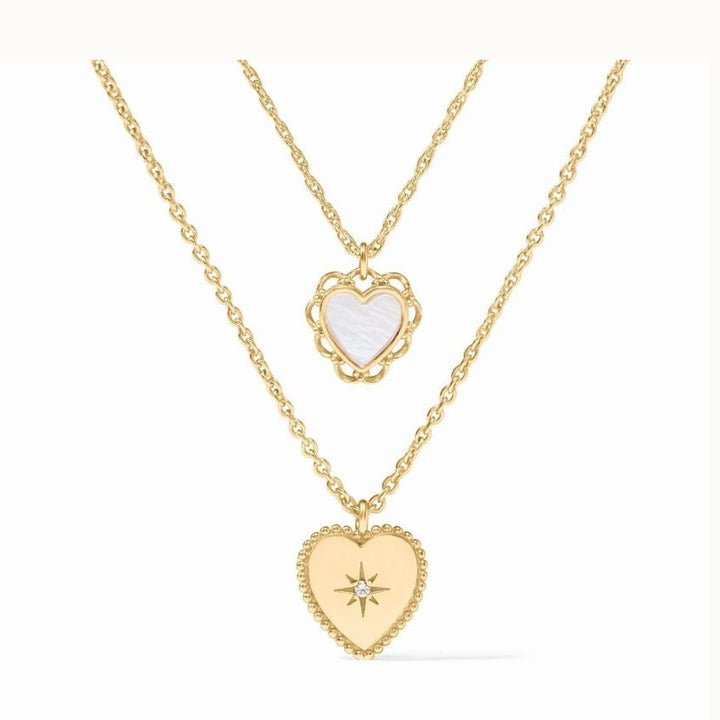Jewelry photography of two layered gold necklaces centered on a white background featuring iconic heart-shaped pendants, a white mother-of-pearl inlay in a scalloped frame, and a central starburst engraving set with a diamond within a beaded border