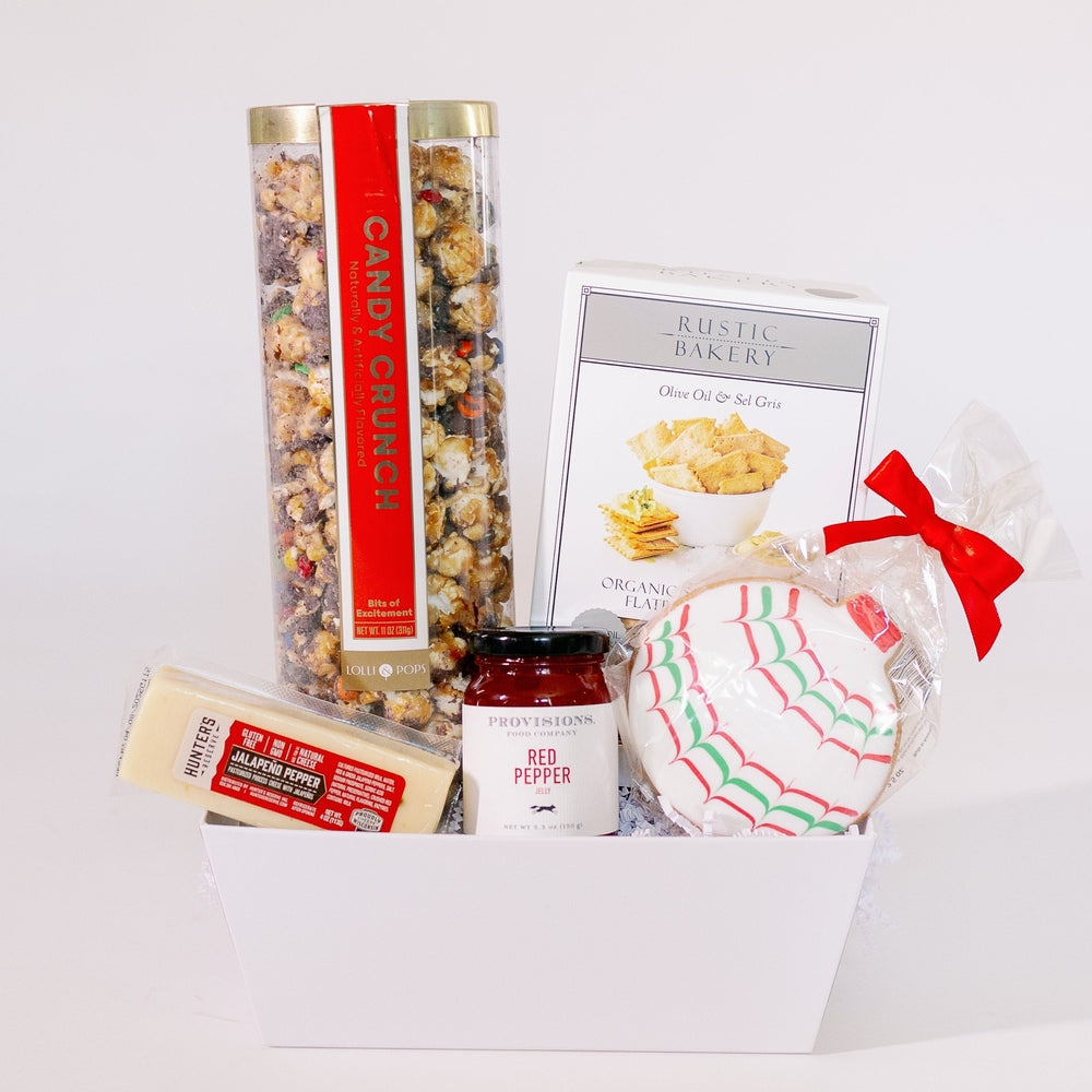 Digital photograph of a gourmet snack gift box in a white container featuring Rustic Bakery crackers, Candy Crunch popcorn, and Hunter's Reserve cheese paired with a festive red-and-green webbed iced cookie tied with a red ribbon and a jar of red pepper jelly