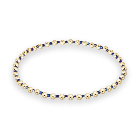 Beaded jewelry bracelet featuring a sequence of polished gold spherical beads and iridescent navy blue spacers arranged in a circular design against a minimalist white background