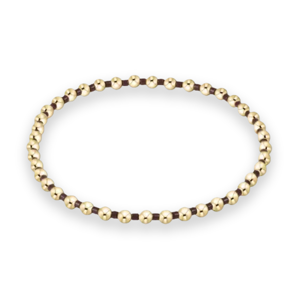 Gold beaded jewelry bracelet featuring a sequence of polished spherical beads and dark brown spacers arranged in a circular silhouette on a neutral off-white studio background