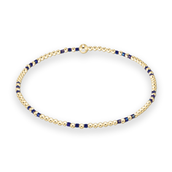 Beaded gold bracelet on a white background featuring small polished gold spheres, interspersed navy blue accents, and a single larger gold bead as a focal point at the top center