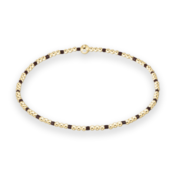 Gold beaded jewelry by an artisan featuring a circular strand of polished yellow gold spheres punctuated by dark brown cylindrical spacers and a single larger gold bead focal point on a white background