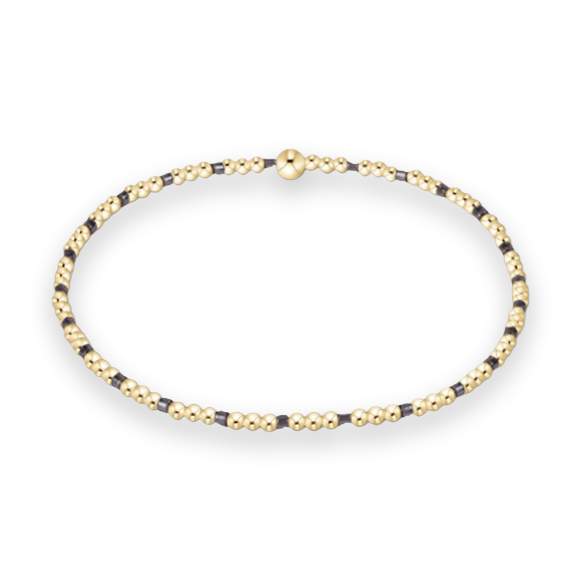 Gold-filled beaded jewelry featuring a repeating pattern of polished gold spheres and dark charcoal square beads centered on a white background with a signature large gold bead focal point