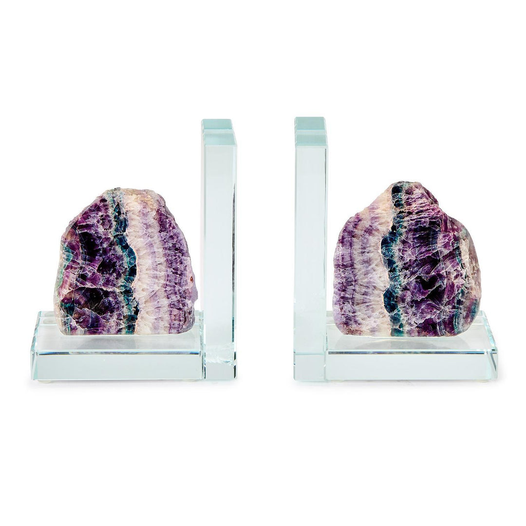 Crystal and fluorite stone bookends on a white background featuring vibrant purple and teal mineral banding, transparent L-shaped glass bases, and raw natural textures