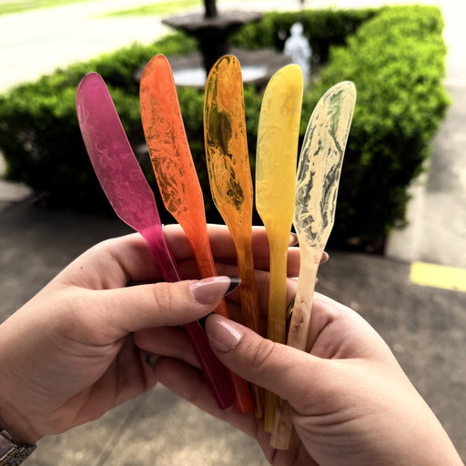 Colorful plastic knives held by a person outdoors with greenery in the background