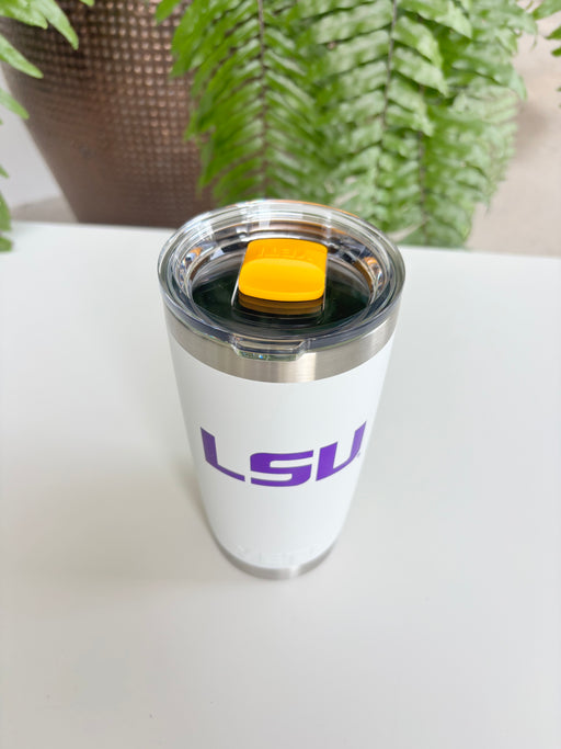 Digital photograph of a white Yeti tumbler featuring a purple LSU logo and a vibrant yellow magnetic slider positioned on a white table against a green fern background