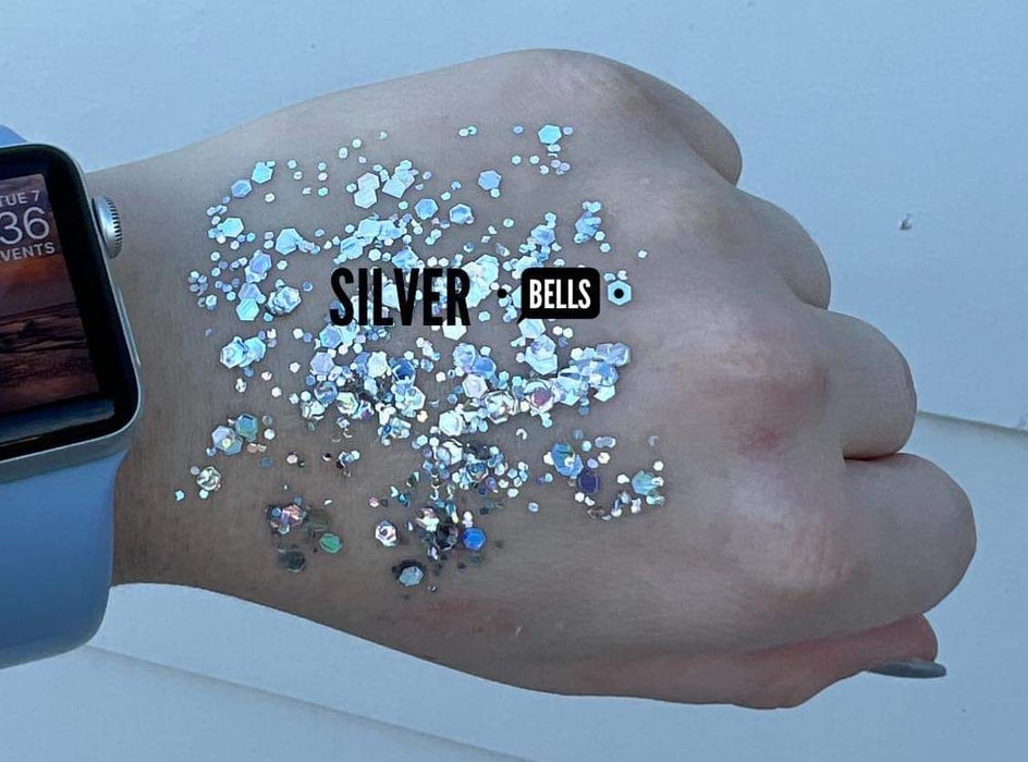 Digital photograph of Silver Bells chunky iridescent glitter swatched on the back of a hand wearing a light blue Apple Watch featuring shimmering hexagonal flakes and vibrant blue reflections