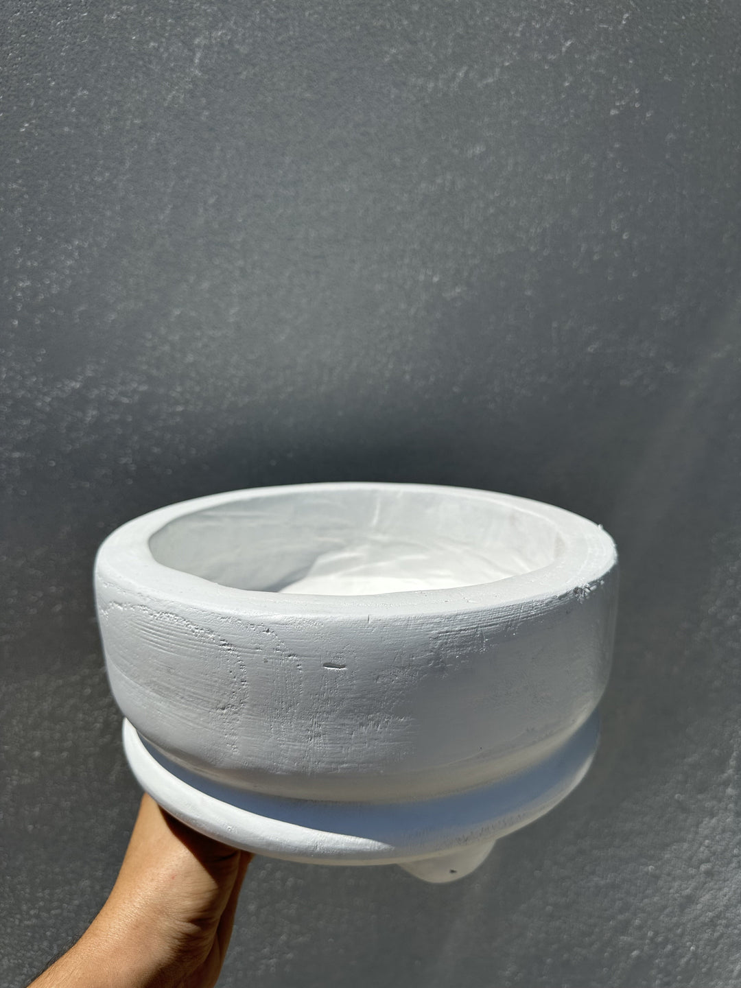 Hand holding a small white-washed footed wood bowl against a gray wall