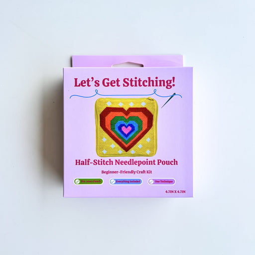 A boxed craft kit labeled "Let's Get Stitching!" and "Half-Stitch Needlepoint Pouch" on a plain white background. The package is light purple with a central illustration of a multicolored heart-shaped needlepoint patch.