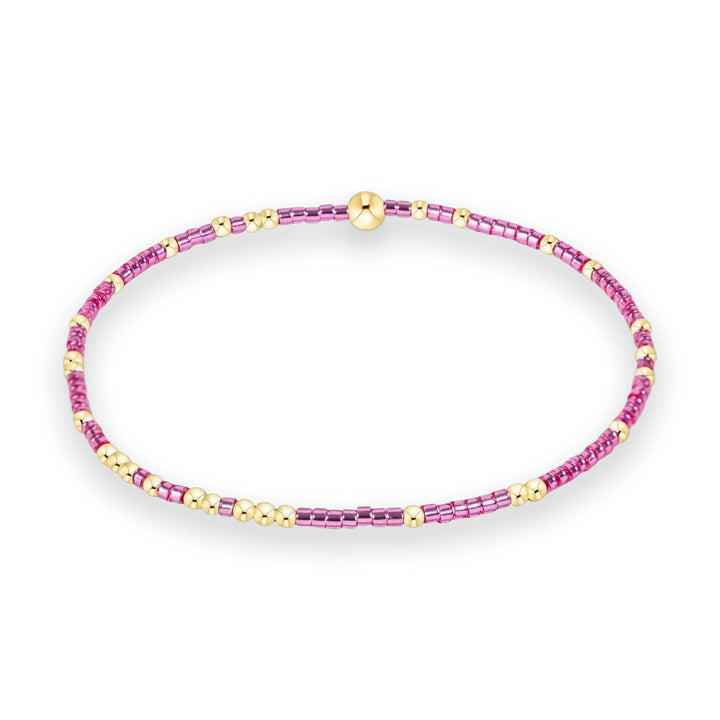 Beaded jewelry bracelet centered on a white background featuring alternating vibrant pink bugle beads, small polished gold spheres, and a single prominent large gold bead at the top
