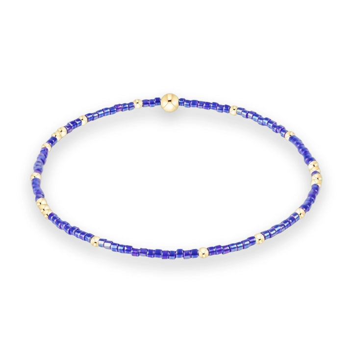 Beaded jewelry featuring a circular bracelet composed of iridescent purple seed beads and polished gold spheres on a white background including a large central gold focal bead and shimmering violet textures