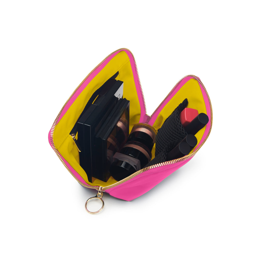 Studio photograph of an open neon pink makeup bag on a white background featuring a bright yellow interior lining, gold-toned ring zipper, and several black cosmetic palettes and lipsticks