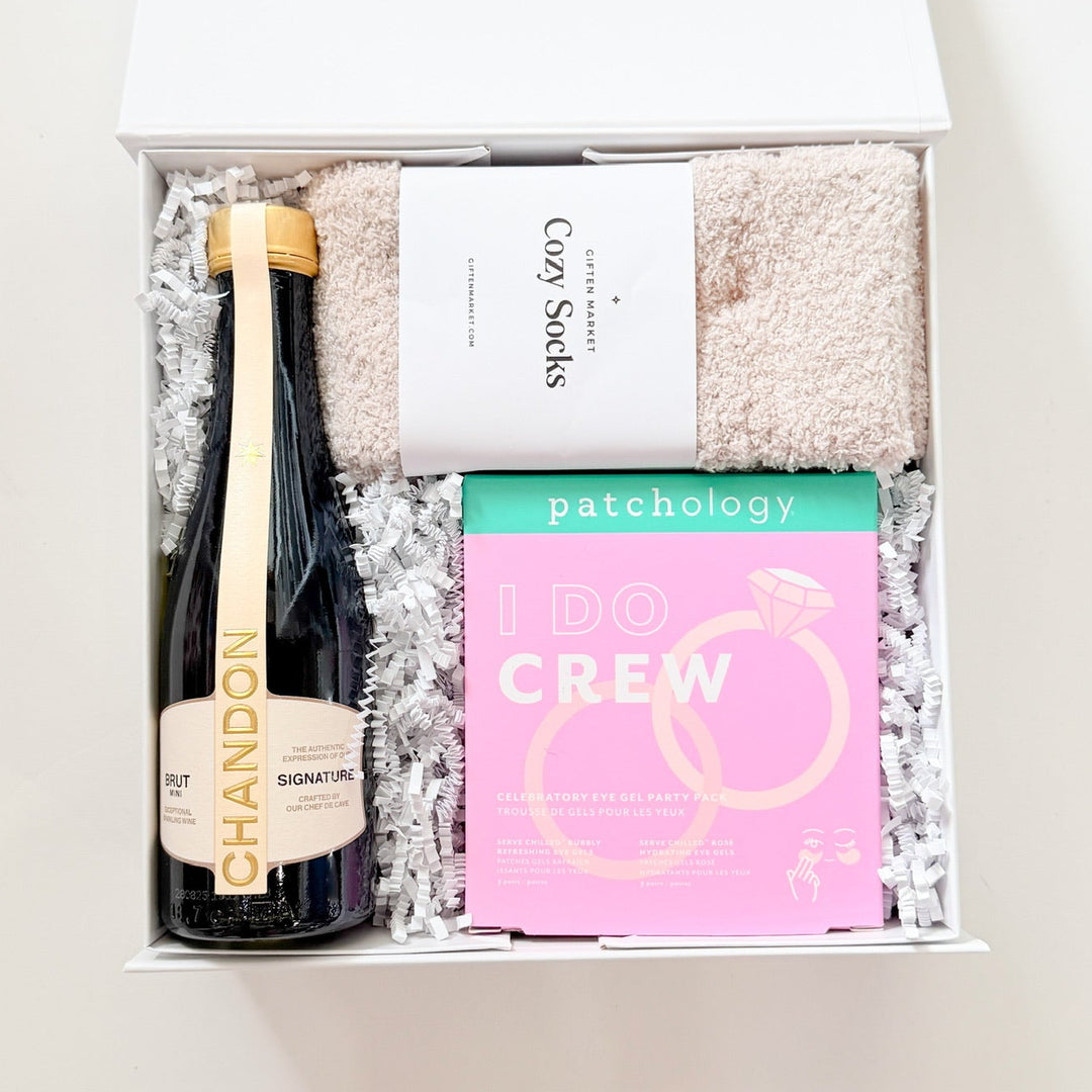 Gift box with a bottle of champagne, bath towels, and a box of patches on a white background