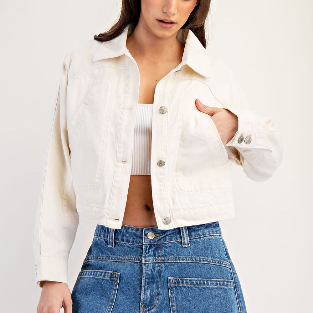 Woman wearing a cream cropped button-front jacket over a white top with blue jeans