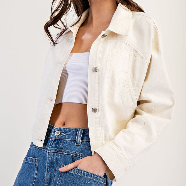 Side view of a woman in a cream cropped jacket with her hand in her jeans pocket