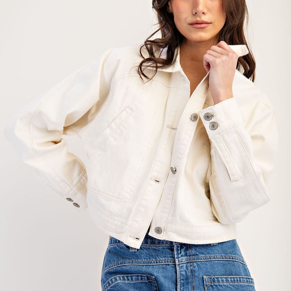 Woman in a buttoned cream cropped jacket holding the collar