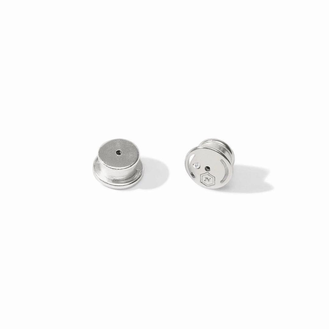 Polished silver metal lapel pin backs by John Varvatos featuring two circular locking clutches on a white background with an engraved hexagonal logo and a small inset clear crystal
