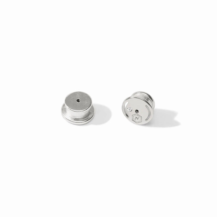 Polished silver metal lapel pin backs by John Varvatos featuring two circular locking clutches on a white background with an engraved hexagonal logo and a small inset clear crystal