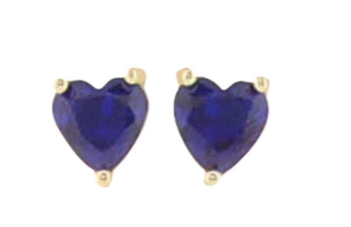 Gold and sapphire jewelry featuring heart-shaped deep blue gemstone stud earrings with a deep indigo hue and three-prong yellow gold settings against a plain white background