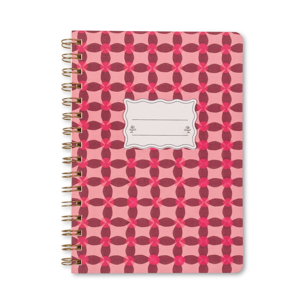 Spiral-bound notebook on a white background featuring a burgundy and pink repeating geometric floral pattern with a metallic gold spiral spine and a central scalloped white label frame