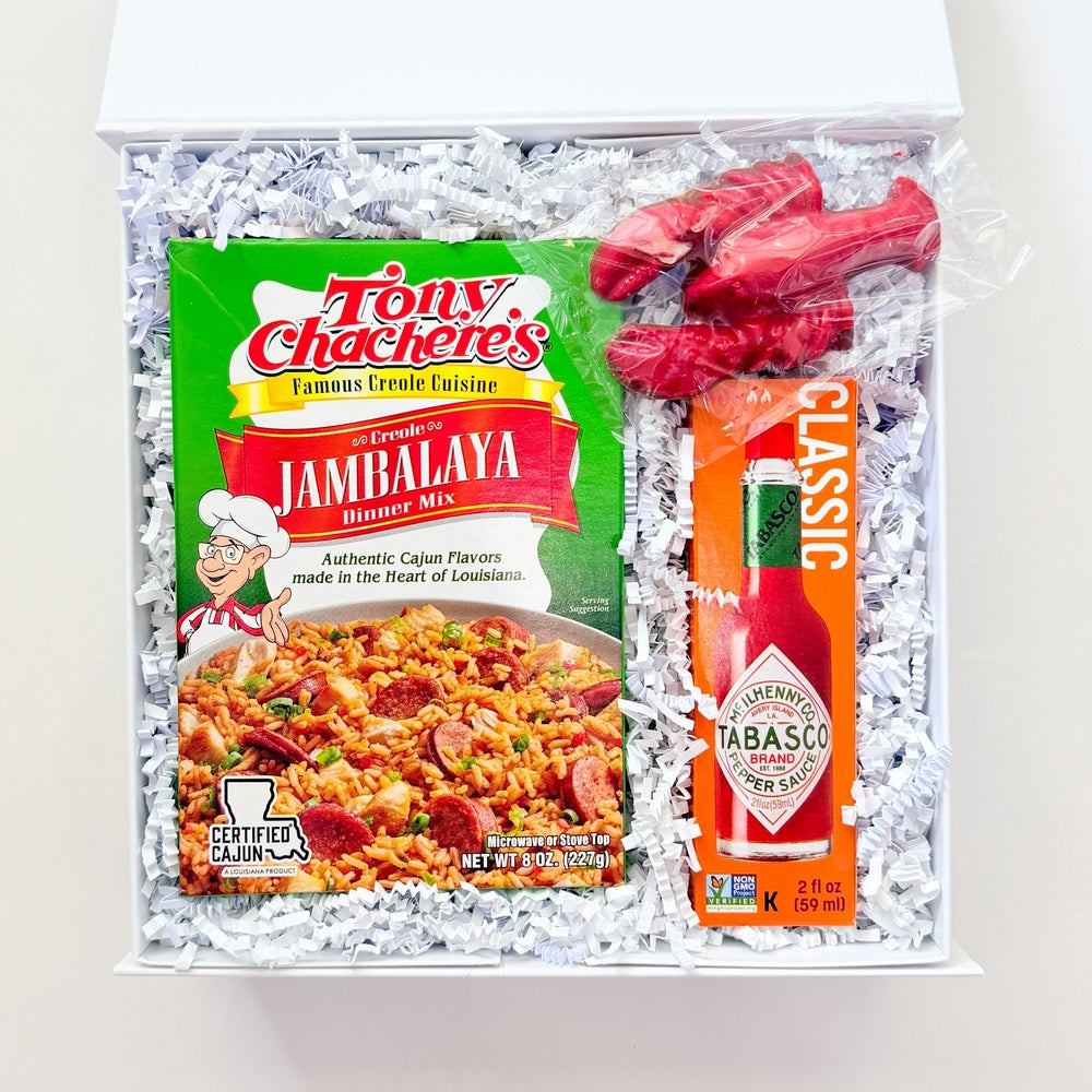 Photograph of a Louisiana gourmet gift box containing iconic Tony Chachere’s and Tabasco products, a bright red crawfish figurine, and a green jambalaya mix box on white shredded paper