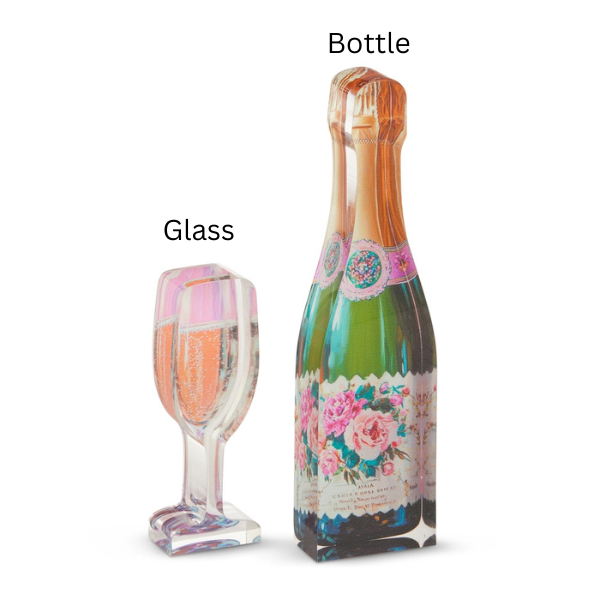 Acrylic glass art sculptures of a champagne bottle and a filled flute glass on a white background featuring a vintage-style floral label with pink roses, a gold-foiled neck, and effervescent bubbles visible through the clear material