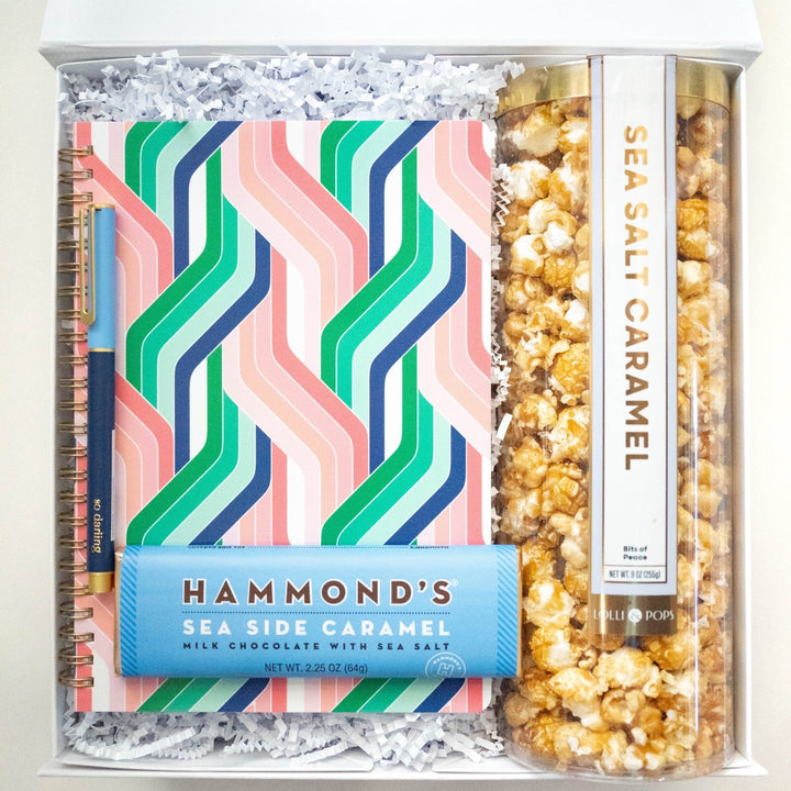 Photograph of a curated gift box featuring a vibrant geometric zigzag notebook, a blue Hammond&